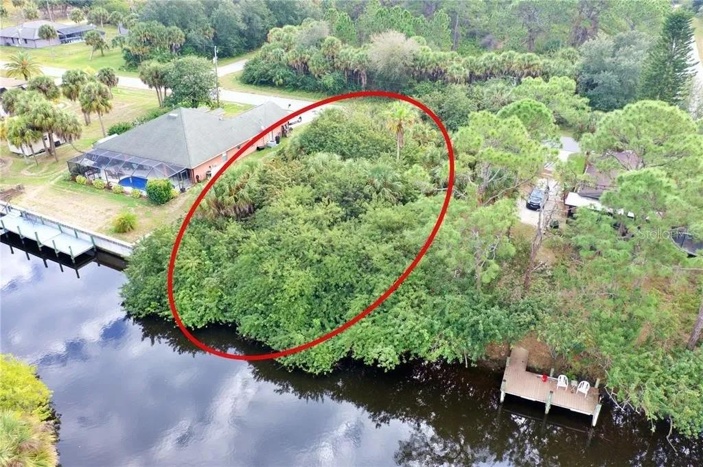 An aerial view shows a wooded, undeveloped waterfront lot circled in red next to a house — 369 CHESHIRE STREET, PORT CHARLOTTE, FL