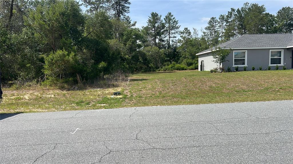A vacant, grassy residential lot sits next to a gray house with a shingled roof — TBD MARION OAKS DRIVE, OCALA, FL