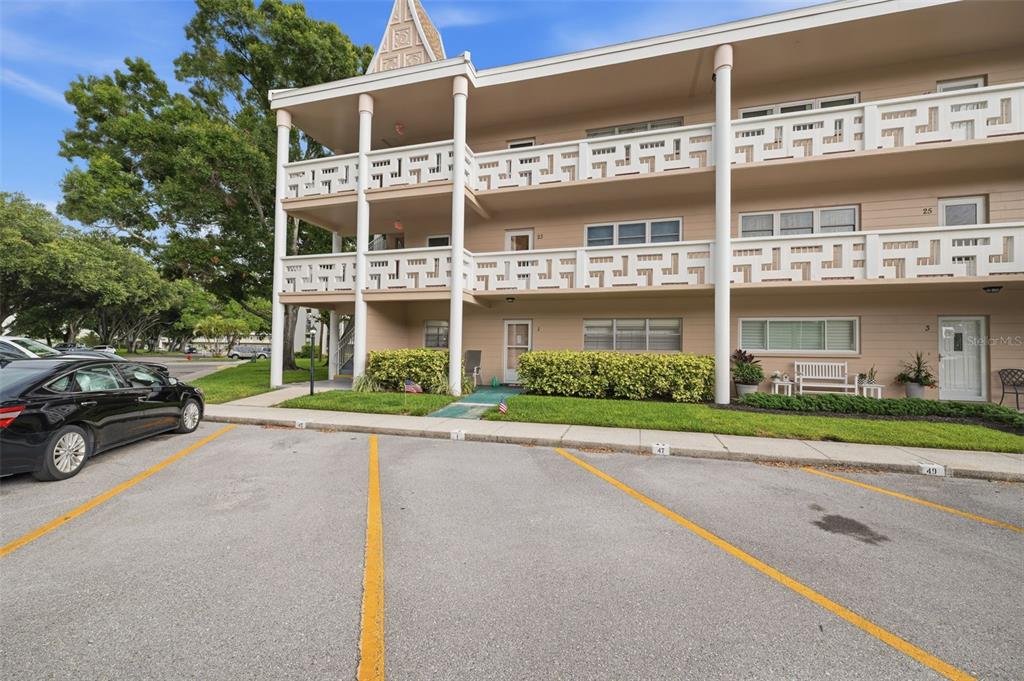 A three-story apartment building features white balconies, tan siding, and a paved parking lot — 2435 SUMATRAN WAY UNIT 23, CLEARWATER, FL