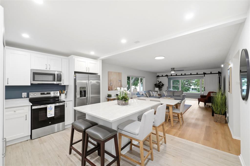 A modern kitchen with white cabinets and a marble island opens into a living area — 2435 SUMATRAN WAY UNIT 23, CLEARWATER, FL