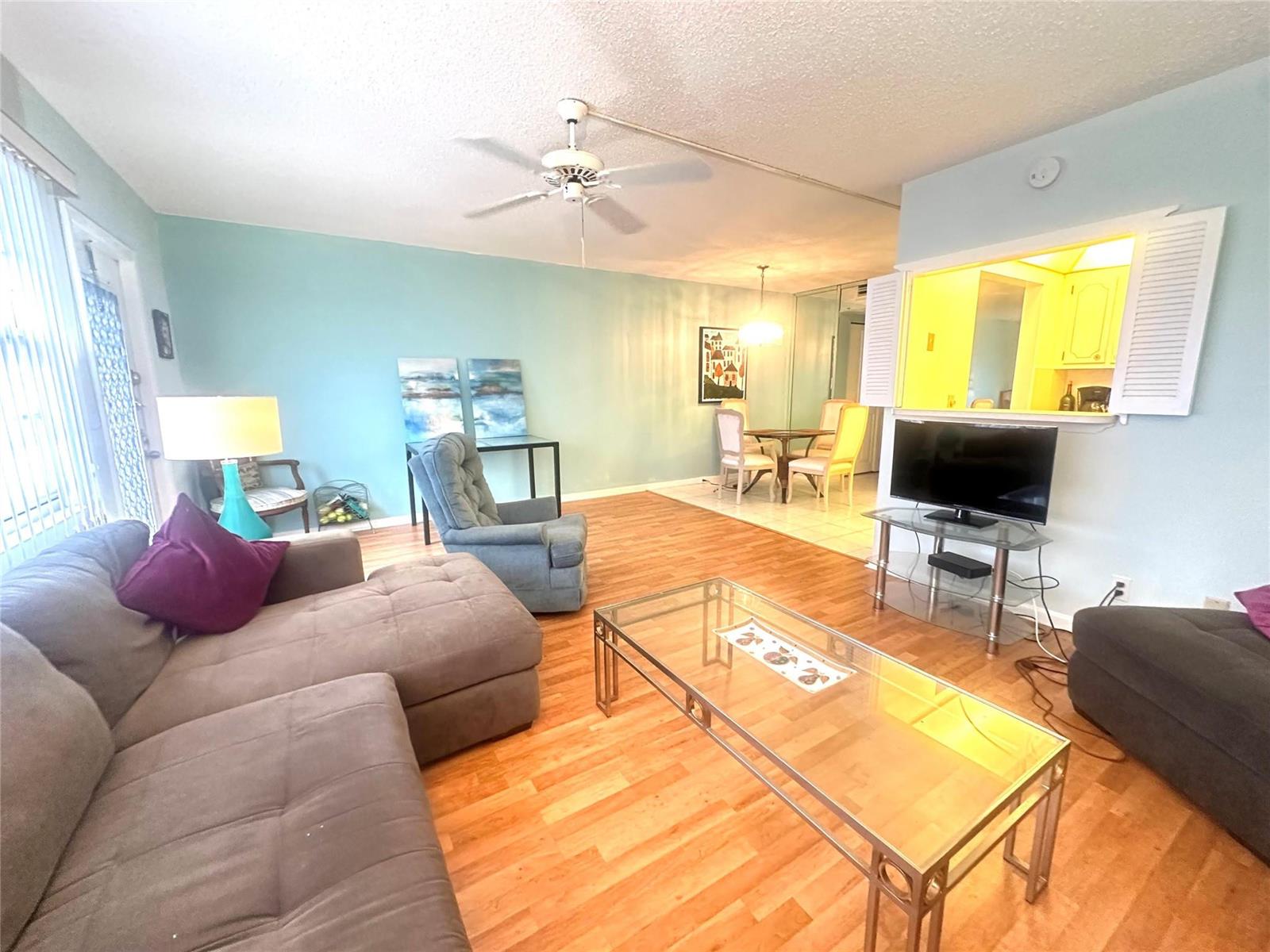 A living room with light blue walls, wood flooring, a glass coffee table, and a sectional — 162 Grantham E # 162, Deerfield Beach FL 33442, DEERFIELD BEACH, FL