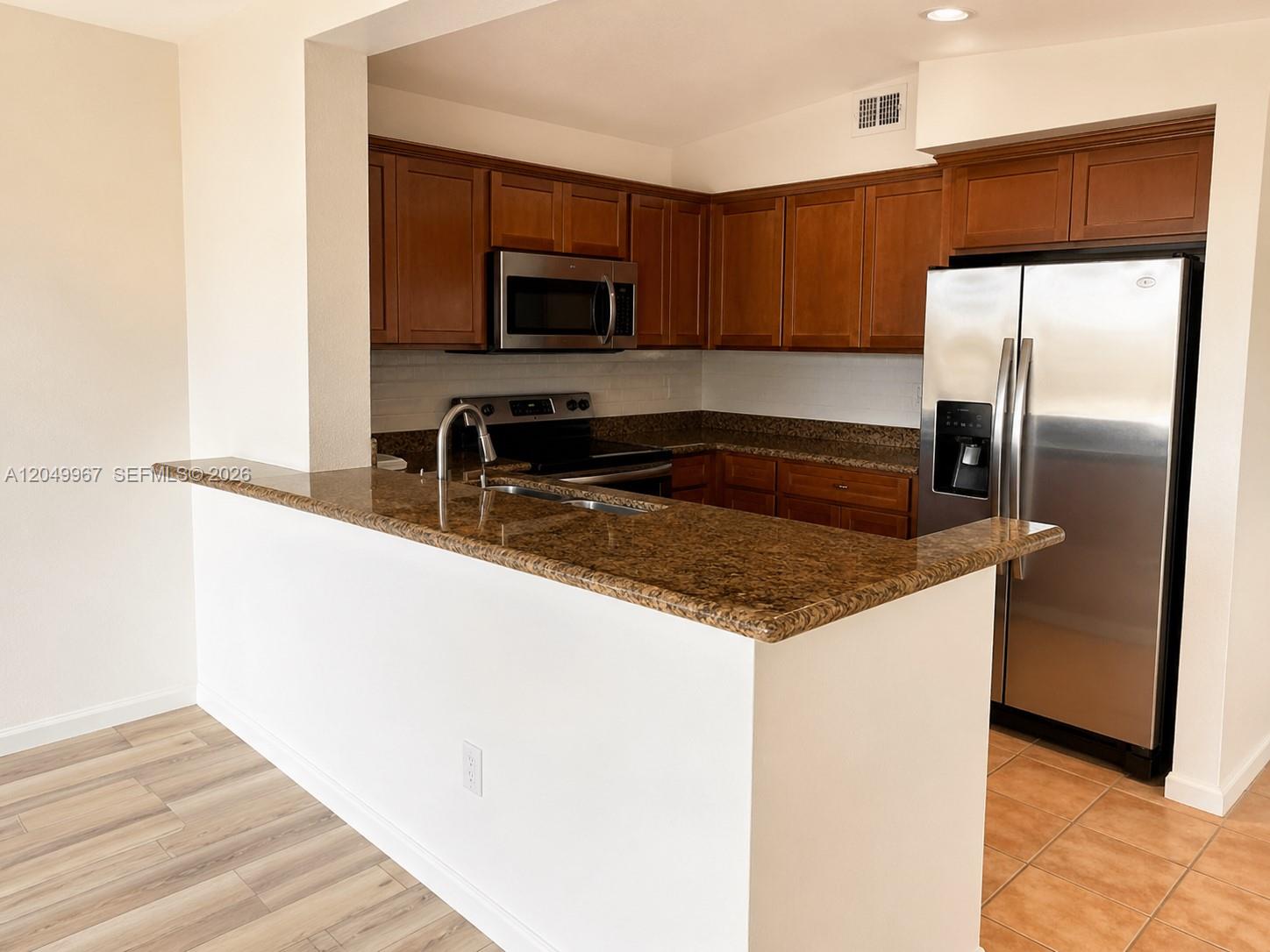 A kitchen features wood cabinets, granite countertops, and stainless steel appliances — 888 S Douglas Rd # 810, Coral Gables FL 33134, CORAL GABLES, FL