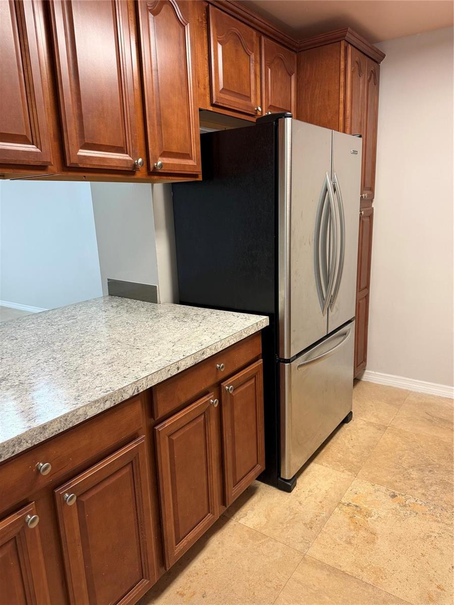 A kitchen features wood cabinets, a stainless steel refrigerator, and a speckled granite countertop — 8601 NW 34th Place # A102, Sunrise FL 33351, SUNRISE, FL