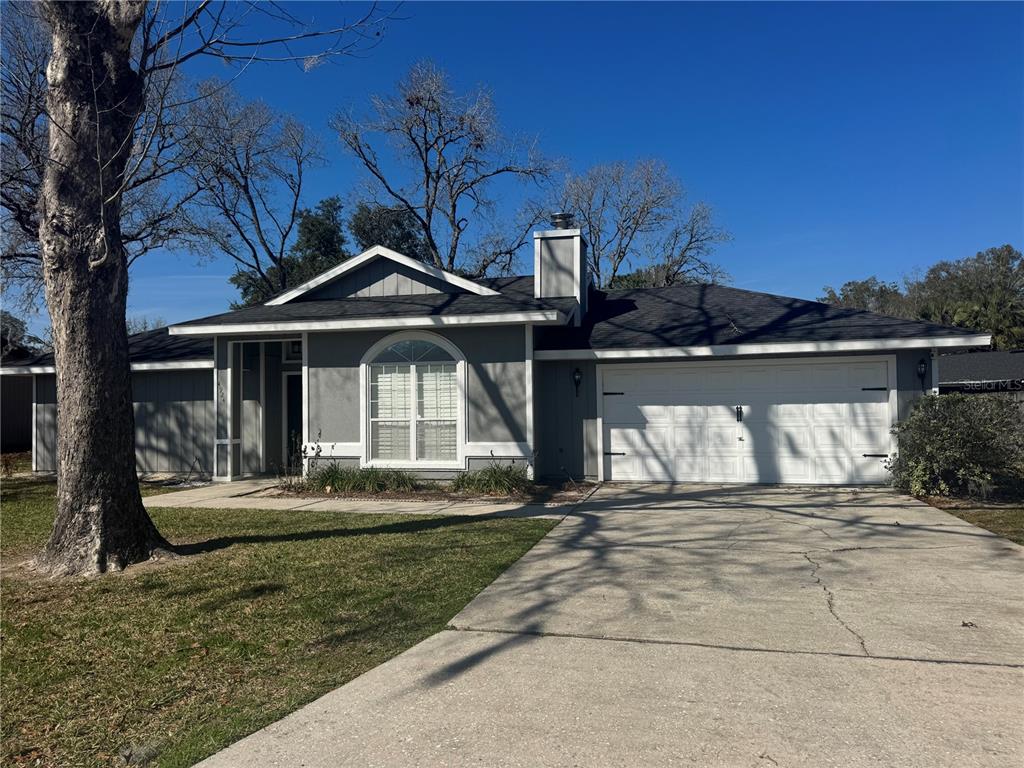 A single-story gray house with a white garage door, arched window, and large front tree — 4924 NW 28TH PLACE, GAINESVILLE, FL