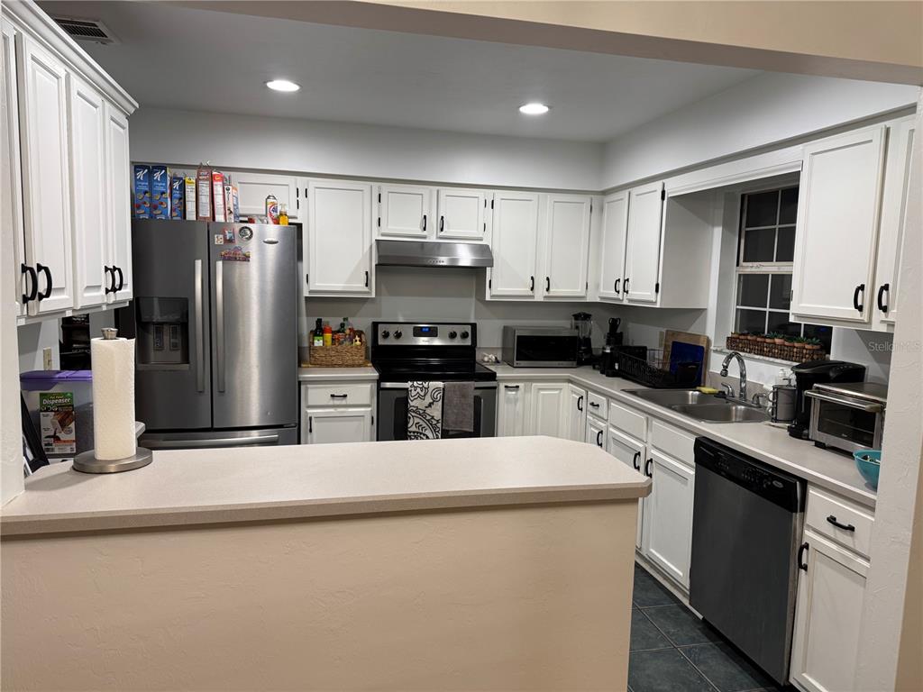 A kitchen features white cabinetry, stainless steel appliances, and a peninsula counter — 4924 NW 28TH PLACE, GAINESVILLE, FL