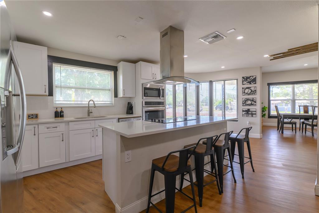 A modern kitchen features white cabinets, a central island with bar stools, and stainless appliances — 800 S KEENE ROAD, CLEARWATER, FL