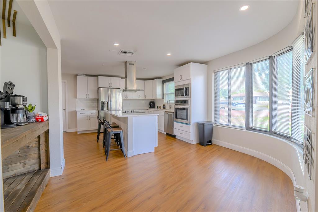 A kitchen features white cabinetry, a central island with bar stools, and large bay windows — 800 S KEENE ROAD, CLEARWATER, FL