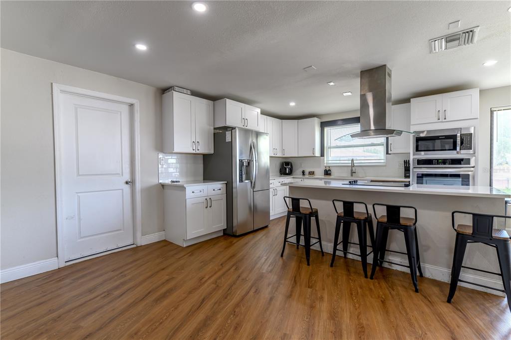 A kitchen features white cabinets, stainless steel appliances, a breakfast bar, and wood-look flooring — 800 S KEENE ROAD, CLEARWATER, FL