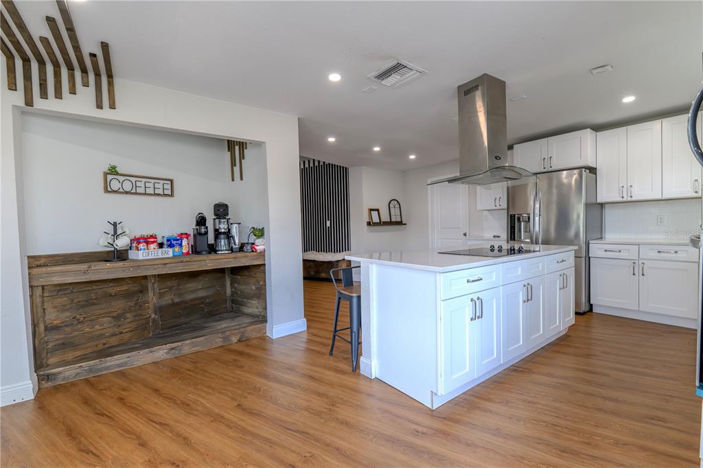 A kitchen features white cabinetry, a central island with a cooktop, and a rustic coffee bar — 800 S KEENE ROAD, CLEARWATER, FL