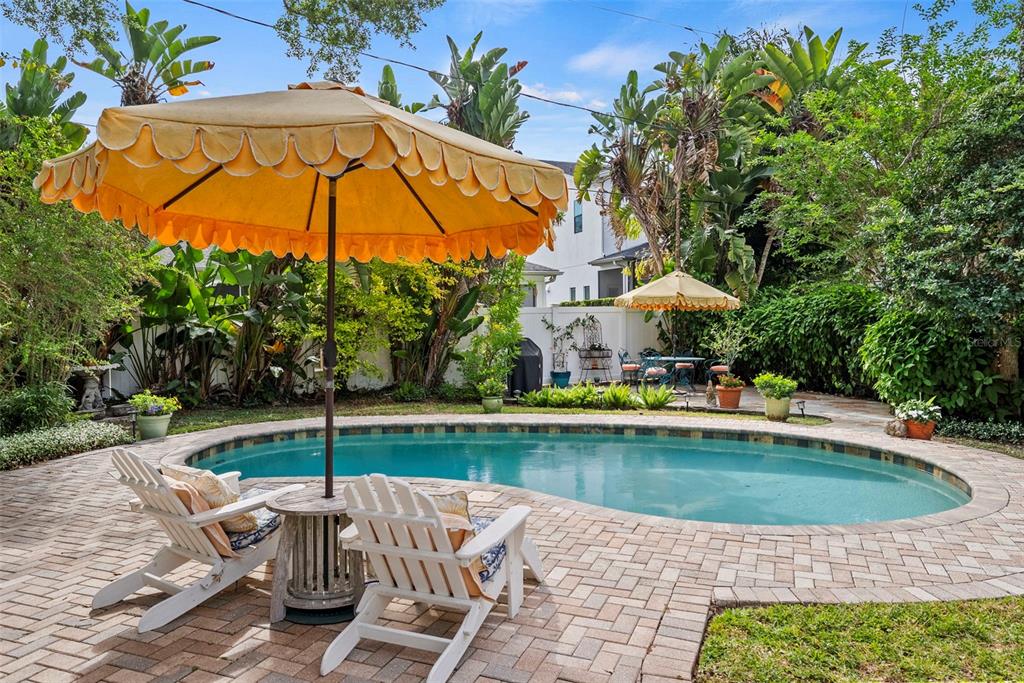 A backyard features a kidney-shaped swimming pool, brick patio, and two white chairs under an umbrella — 212 S COOLIDGE AVENUE, TAMPA, FL