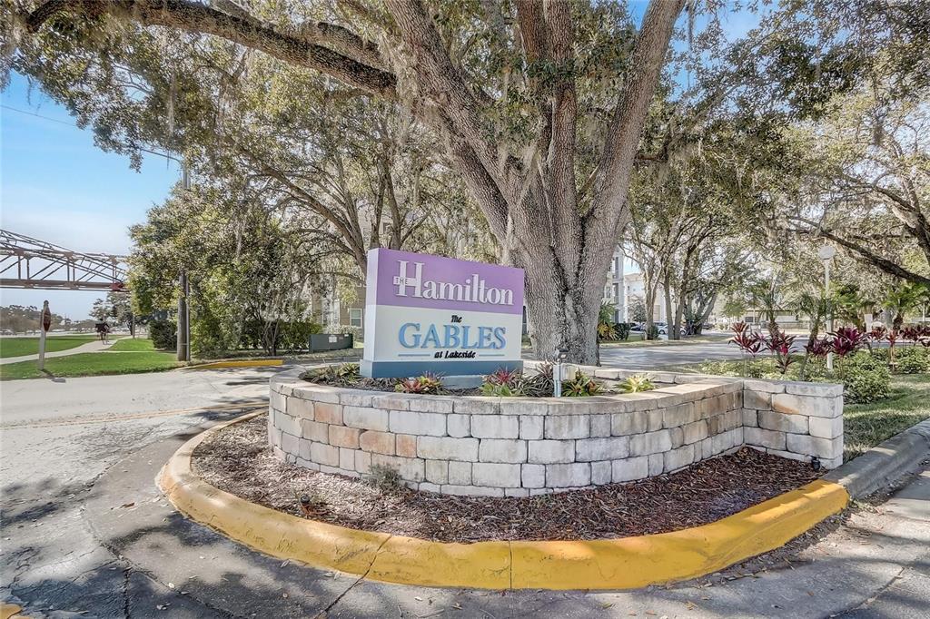 A stone-walled sign for The Gables at Lakeside sits beneath a large tree — 1229 BERMUDA LAKES LANE UNIT 202, KISSIMMEE, FL