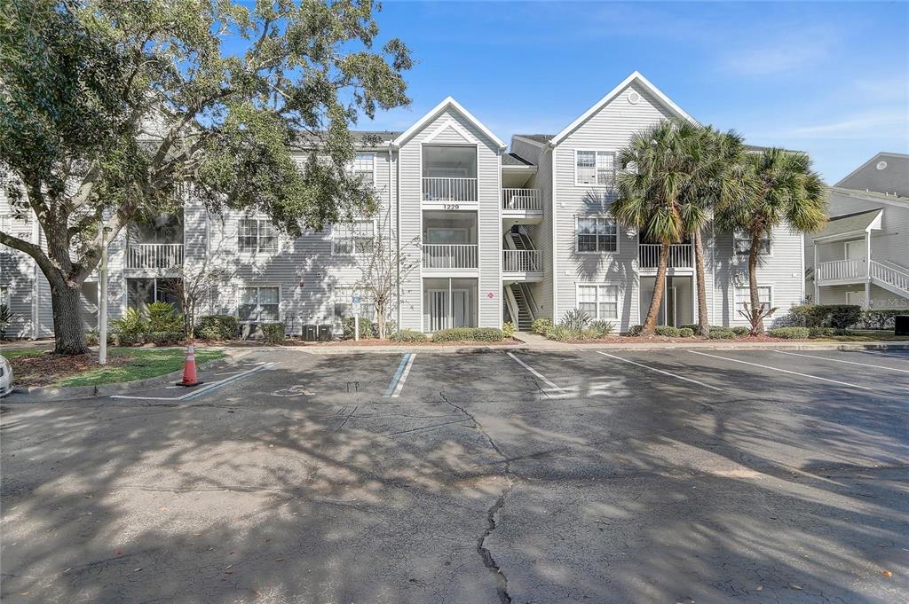A three-story apartment building with light siding and a parking lot in the foreground — 1229 BERMUDA LAKES LANE UNIT 202, KISSIMMEE, FL