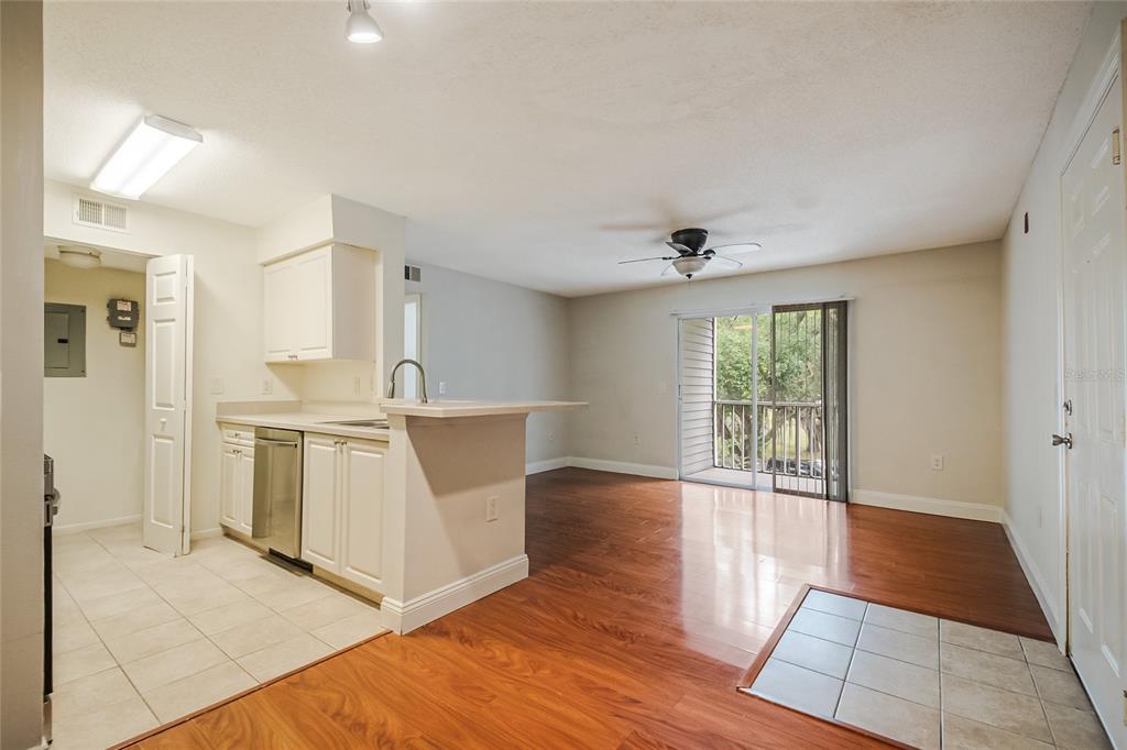 An open-concept living area with wood flooring, a kitchen with white cabinets, and sliding doors — 1229 BERMUDA LAKES LANE UNIT 202, KISSIMMEE, FL