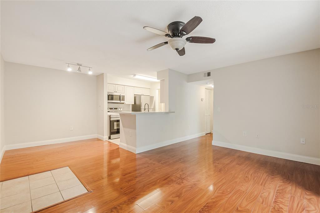 A living room with wood-look flooring opens to a kitchen featuring a breakfast bar — 1229 BERMUDA LAKES LANE UNIT 202, KISSIMMEE, FL