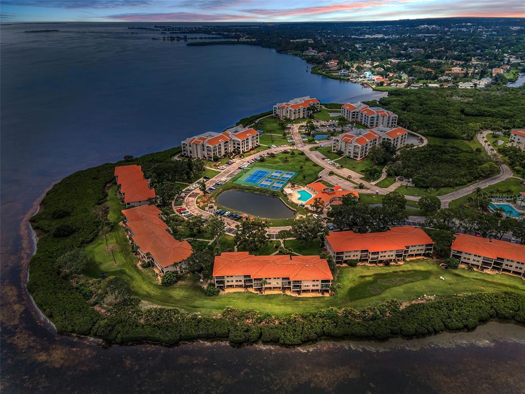 An aerial view of a waterfront residential complex with multiple buildings, a pool, and courts — 1813 MARINER DRIVE UNIT 146, TARPON SPRINGS, FL