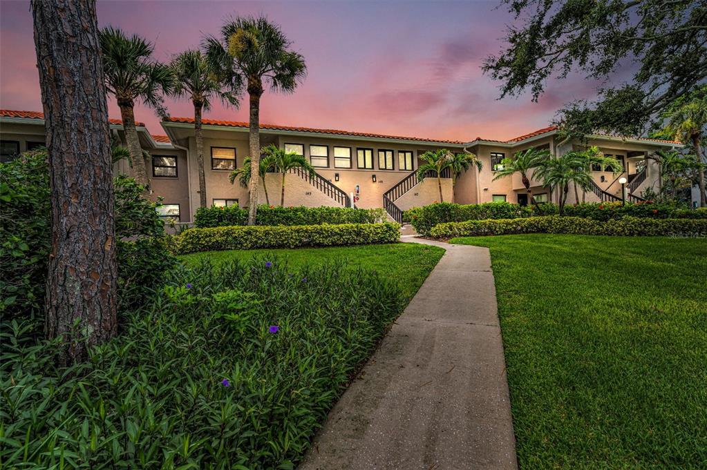 A concrete walkway leads toward a two-story apartment building with palm trees and landscaping — 1813 MARINER DRIVE UNIT 146, TARPON SPRINGS, FL