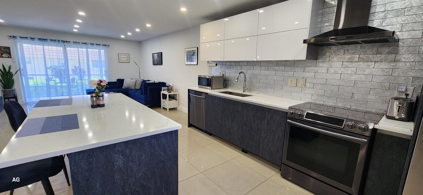 A modern kitchen features dark textured lower cabinets, white upper cabinets, and a large island — 20 SE 13th Street # B7, Boca Raton FL 33432, BOCA RATON, FL