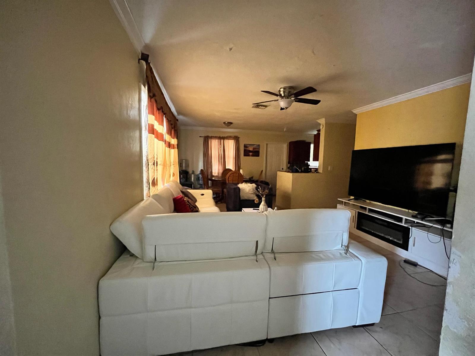A living room features a white sectional sofa, a large television, and a ceiling fan — 4730 NE 2nd Avenue NE, Deerfield Beach FL 33064, DEERFIELD BEACH, FL