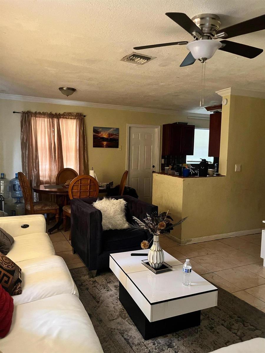 A living room with a white sofa, dark armchair, coffee table, and adjacent dining area — 4730 NE 2nd Avenue NE, Deerfield Beach FL 33064, DEERFIELD BEACH, FL