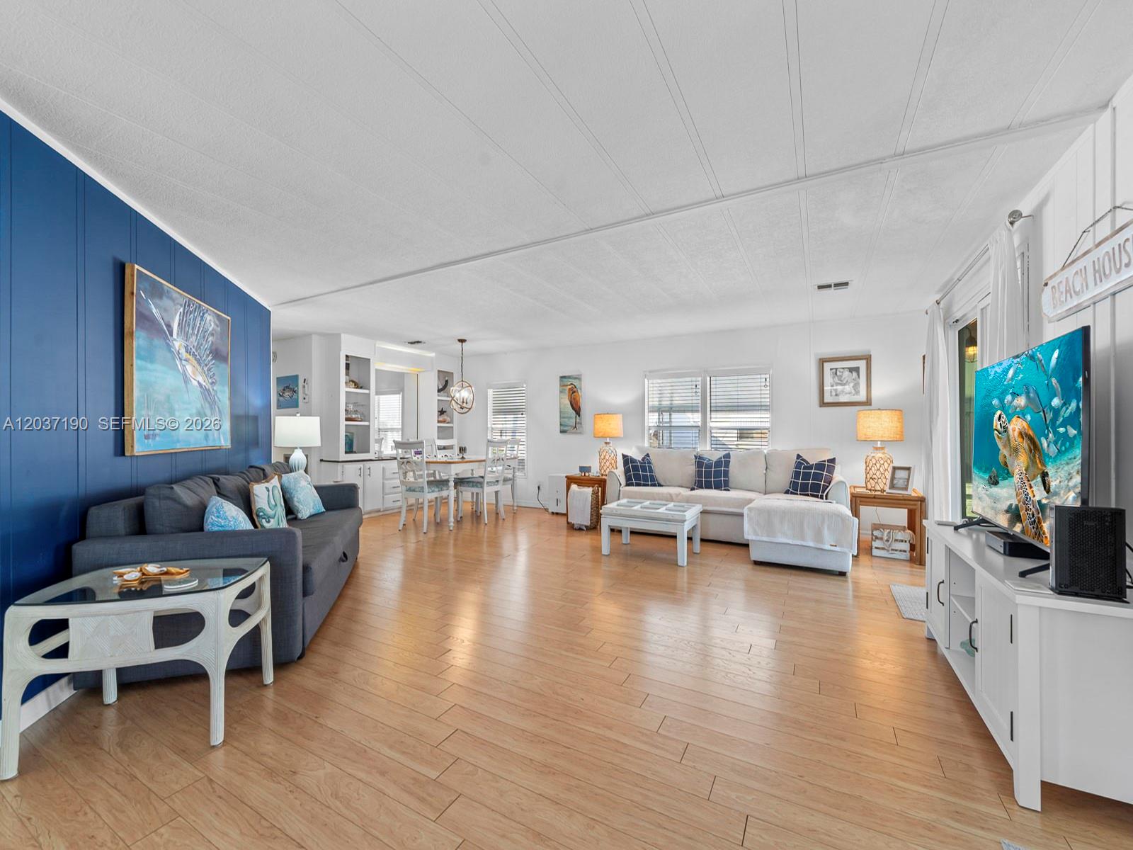 A spacious living and dining area features light wood flooring, a blue accent wall, and furniture — 806 S Jade Dr # 806, Key Largo FL 33037, KEY LARGO, FL