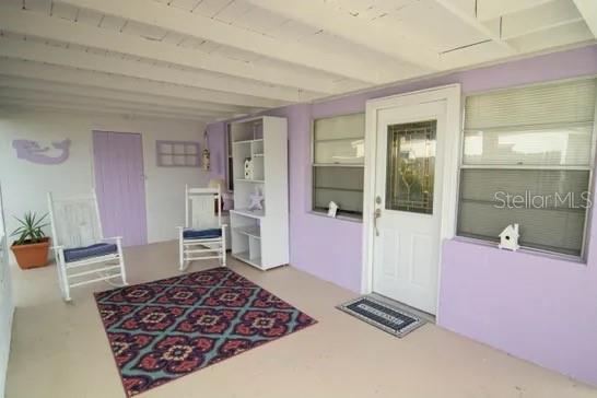 A covered porch with purple walls, two rocking chairs, a white shelving unit, and rug — 121 LAURIE DRIVE, ORMOND BEACH, FL