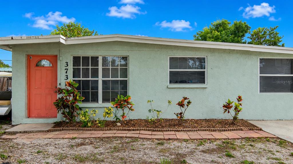 A light green single-story house features a coral-colored front door and a small garden bed — 3731 PAPAI DRIVE, SARASOTA, FL