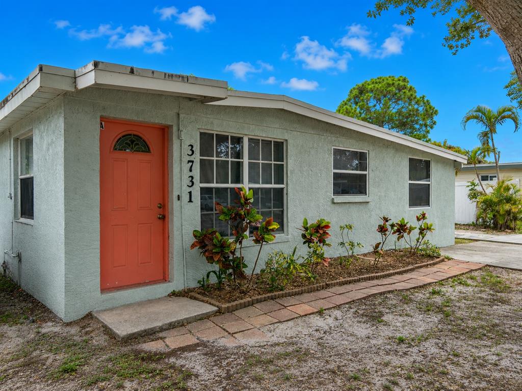A light green, single-story house features a coral-colored front door and a small garden bed — 3731 PAPAI DRIVE, SARASOTA, FL