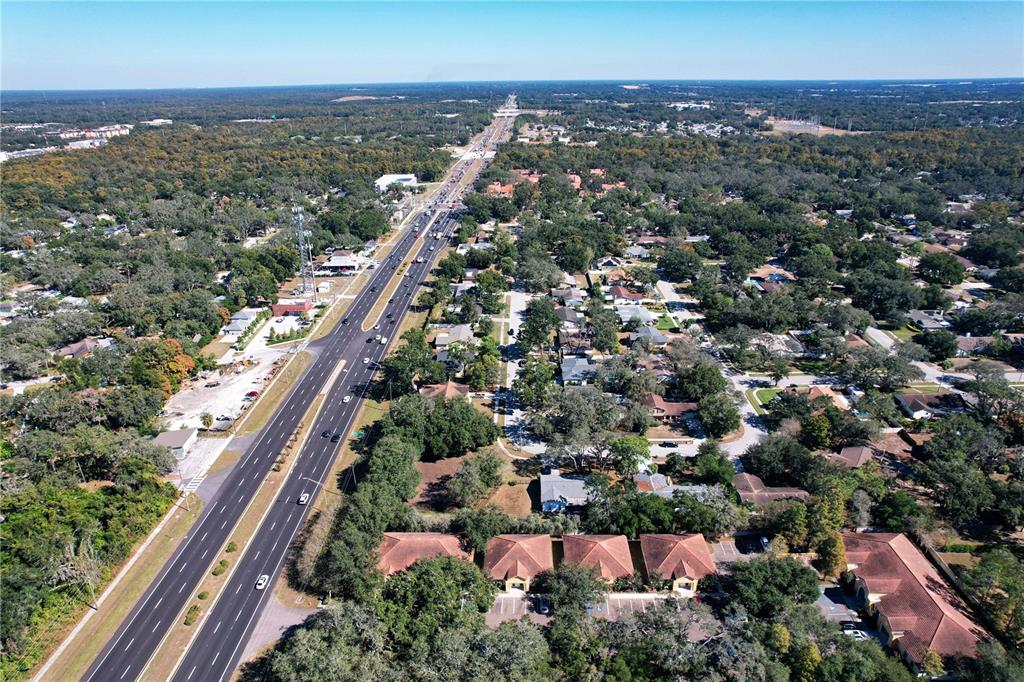 An aerial view shows a multi-lane highway running through a suburban area with wooded lots — 6957 E FOWLER AVENUE, TAMPA, FL