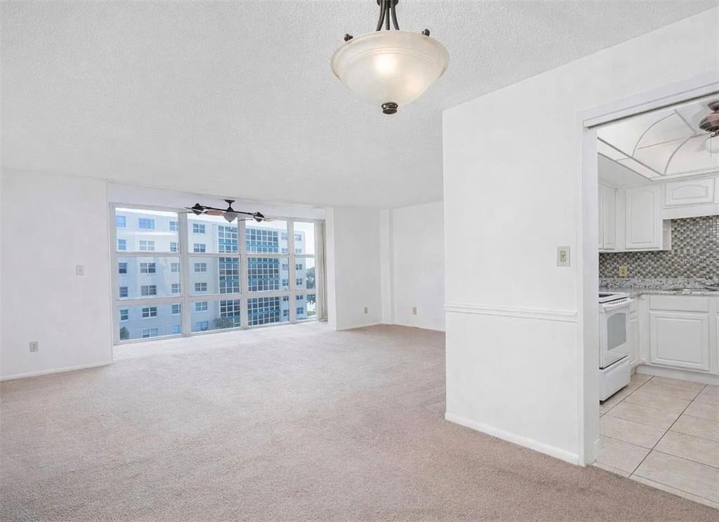 A carpeted living room with a large window and an adjacent kitchen with white cabinets — 1224 S PENINSULA DRIVE UNIT 415, DAYTONA BEACH, FL