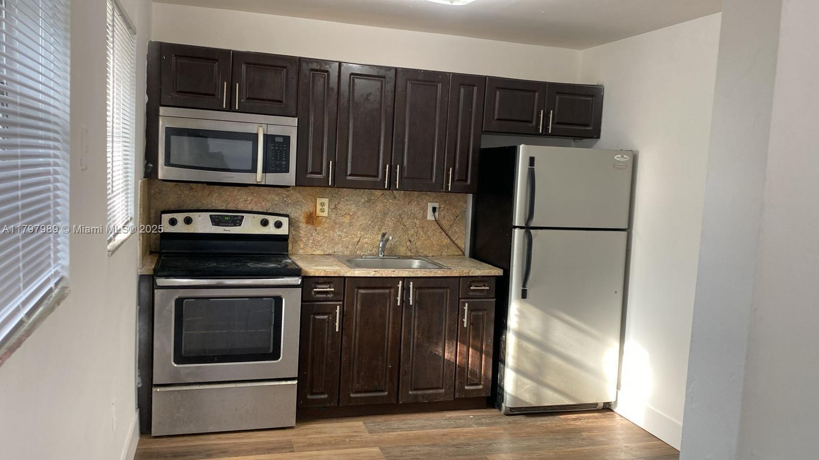 A kitchen features dark wood cabinets, stainless steel appliances, and a stone-look backsplash — 1173 NW 65th St, Miami FL 33150, MIAMI, FL