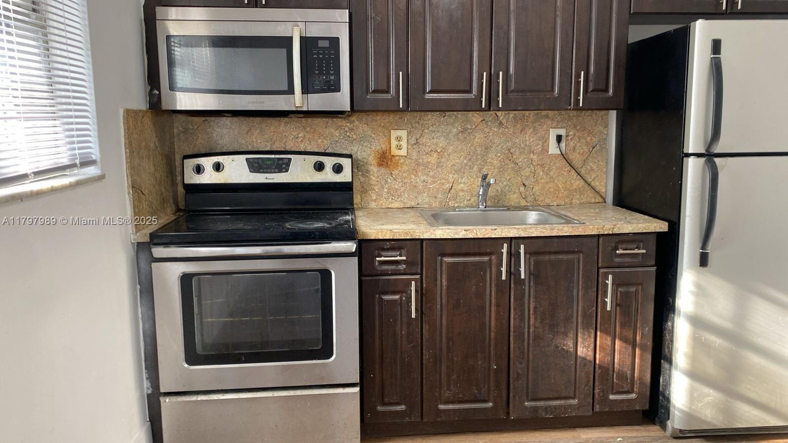 A kitchen features dark wood cabinets, stainless steel appliances, and a stone-look backsplash — 1173 NW 65th St, Miami FL 33150, MIAMI, FL