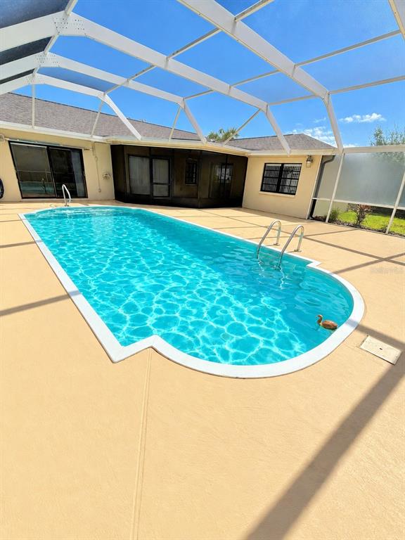 A swimming pool with a metal ladder sits inside a screened-in patio area — 2801 NARCISSUS DRIVE, HOLIDAY, FL