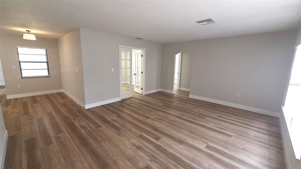 An empty room features light wood-look flooring, gray walls, French doors, and an arched doorway — 2801 NARCISSUS DRIVE, HOLIDAY, FL