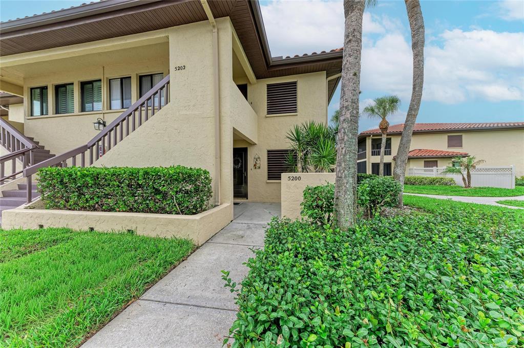 An exterior view of a two-story stucco apartment building with a staircase and landscaping — 5200 LAKE VILLAGE DRIVE UNIT 79, SARASOTA, FL