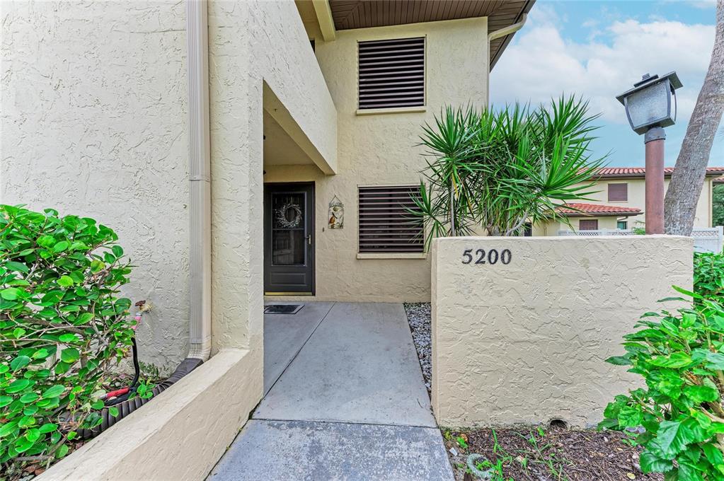 A concrete walkway leads to the front entrance of a two-story stucco townhouse — 5200 LAKE VILLAGE DRIVE UNIT 79, SARASOTA, FL