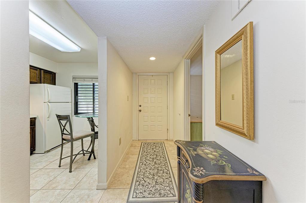 A tiled entryway features a white front door, a decorative console table, and a mirror — 5200 LAKE VILLAGE DRIVE UNIT 79, SARASOTA, FL