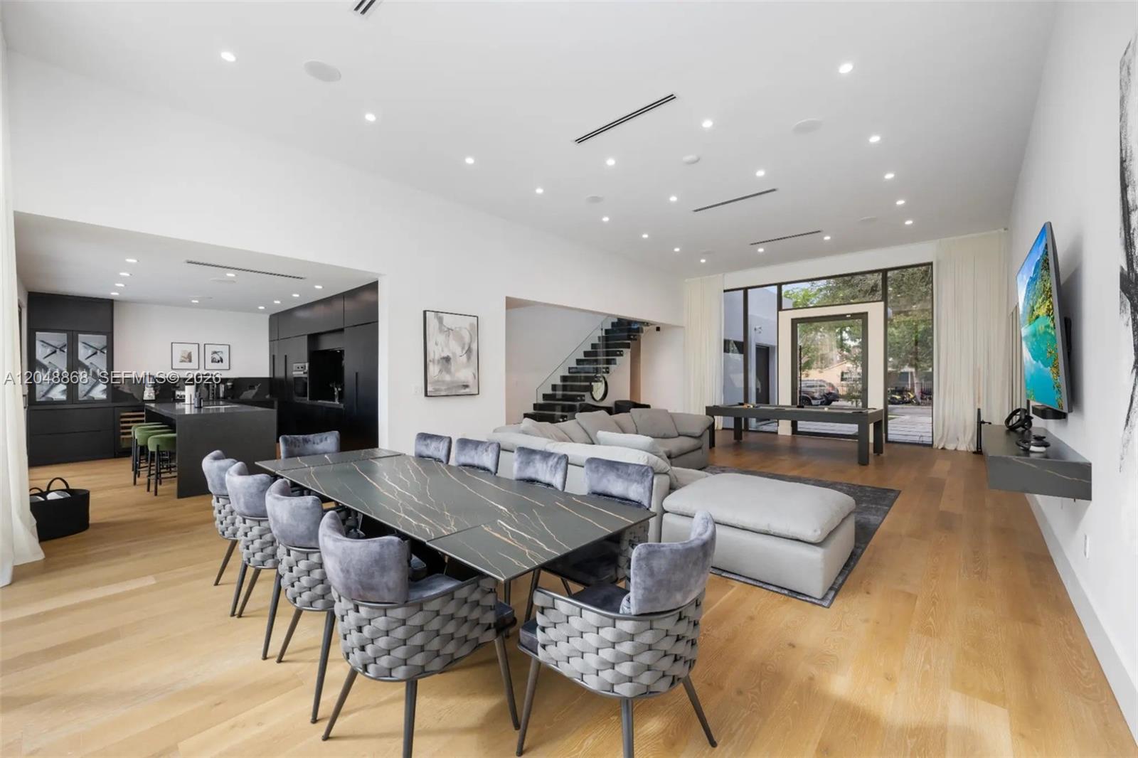 An open-concept living and dining area features a dark marble table, sectional sofa, and kitchen — 80 NW 45th St, Miami FL 33127, MIAMI, FL