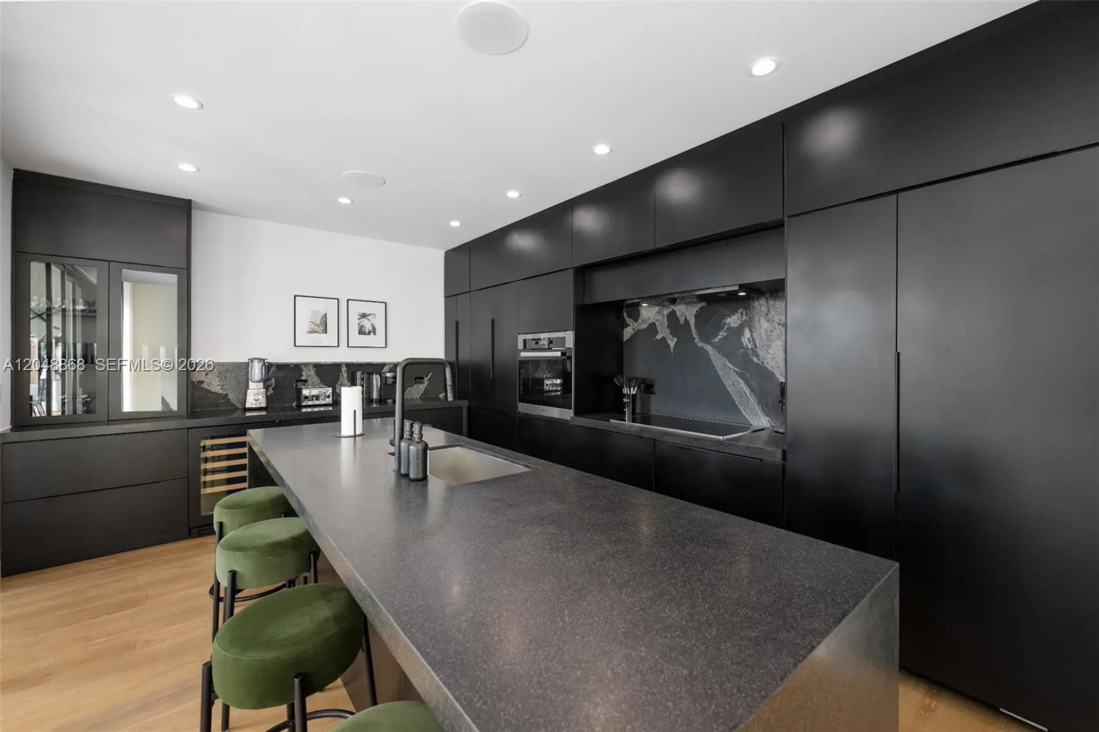 A modern kitchen features matte black cabinetry, a large stone island, and green velvet stools — 80 NW 45th St, Miami FL 33127, MIAMI, FL