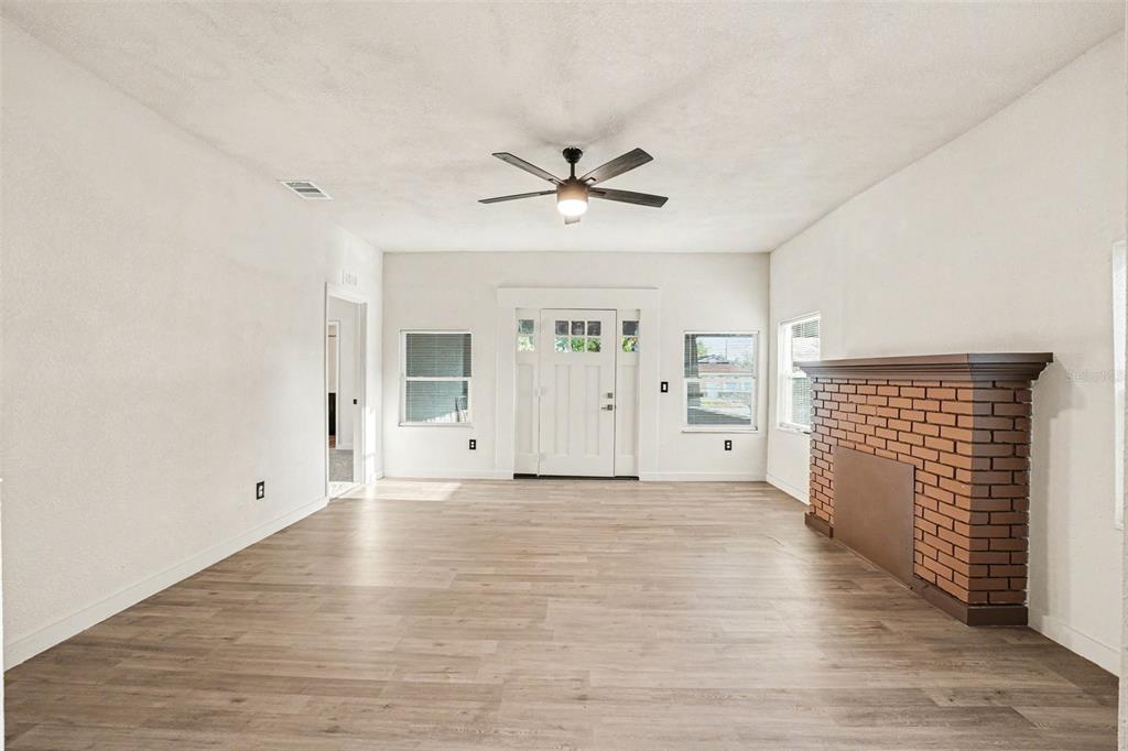 A living room with light wood-look flooring, a brick fireplace, and a ceiling fan — 129 W PARK AVENUE, LAKE WALES, FL