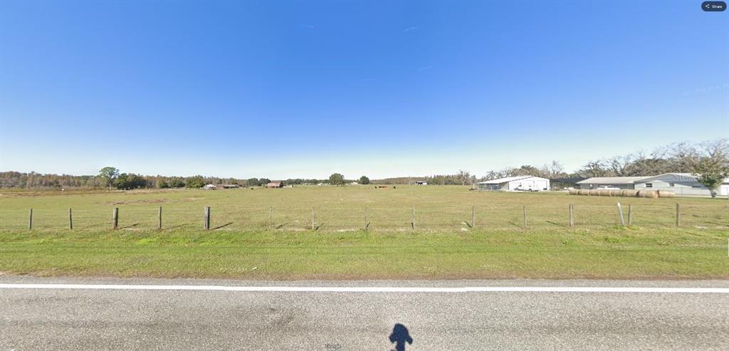 A wide, flat, grassy field is enclosed by a wire fence along a paved road — OLD POLK CITY RD, POLK CITY, FL