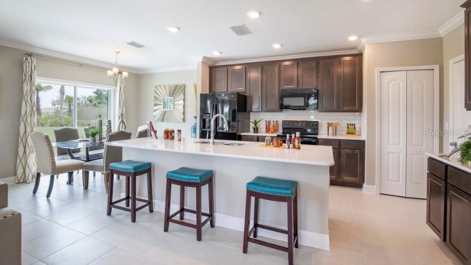 A kitchen features dark wood cabinets, a white island with teal stools, and dining area — 3828 BLUETHREAD WAY, POINCIANA, FL