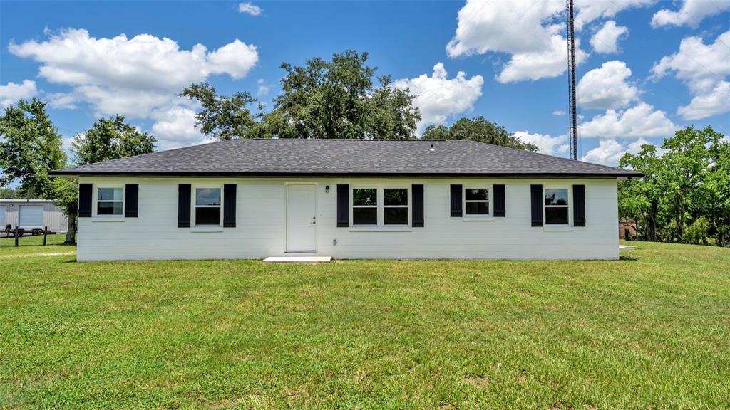 A single-story white house with black shutters and a dark shingled roof under blue skies — 11637 US HIGHWAY 98 N, LAKELAND, FL
