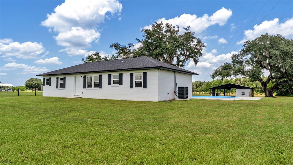 A white, single-story house with a dark roof sits on a large, grassy lot — 11637 US HIGHWAY 98 N, LAKELAND, FL