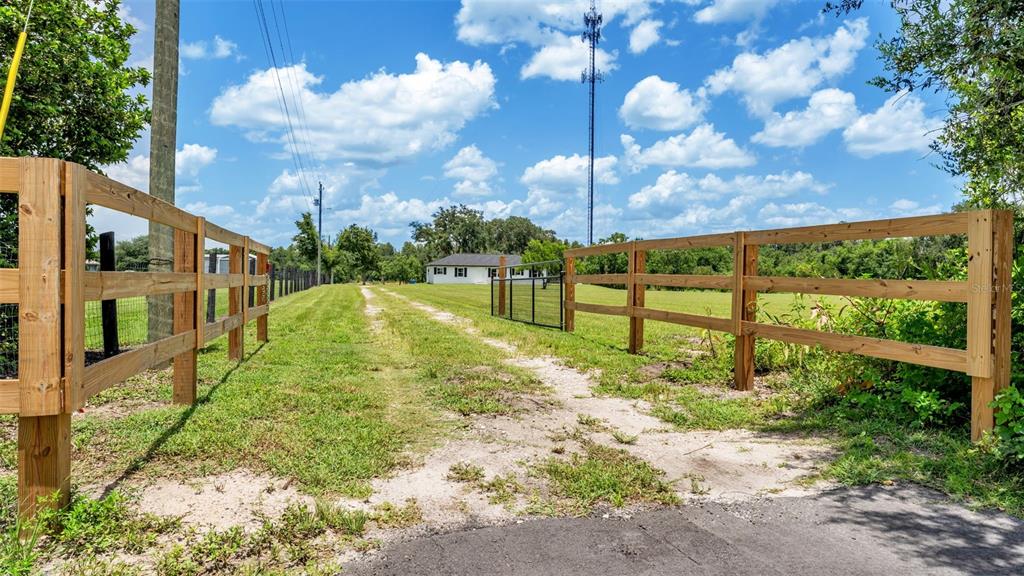 A dirt driveway leads through a wooden fence toward a white house under a blue sky — 11637 US HIGHWAY 98 N, LAKELAND, FL