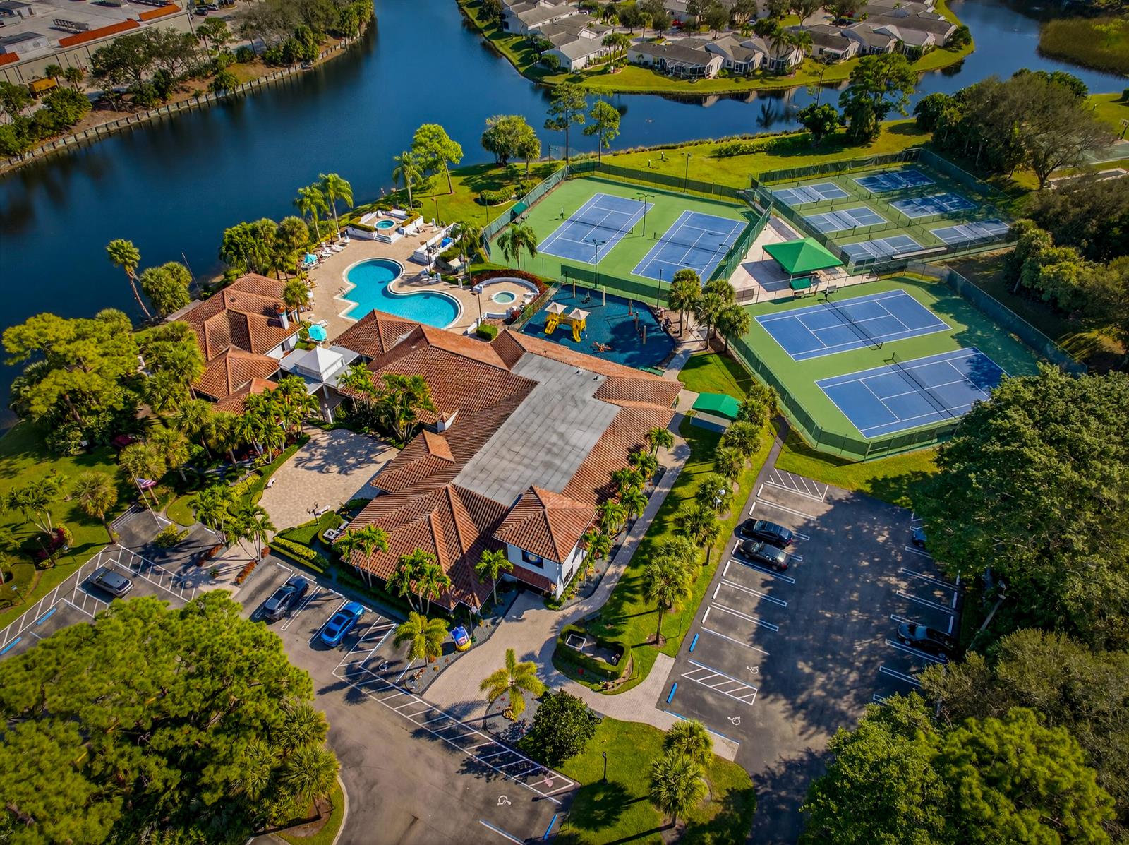 An aerial view shows a clubhouse with a pool, tennis courts, and parking lot — 113 Egret Circle, FL 33413, FL