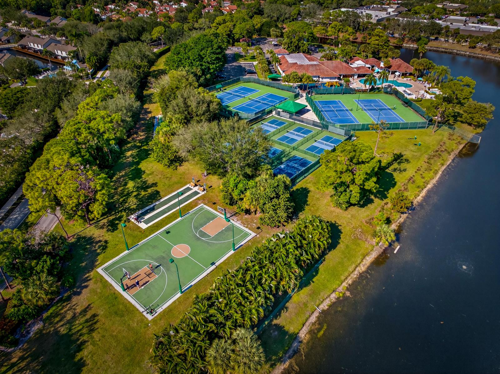 An aerial view shows a basketball court, tennis courts, and a swimming pool near a lake — 113 Egret Circle, FL 33413, FL