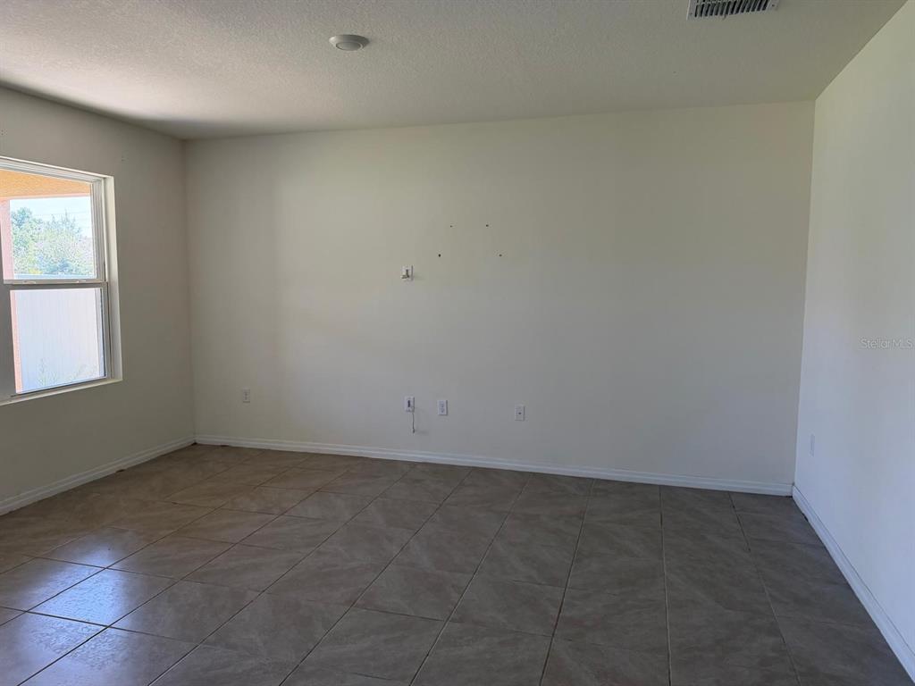 An empty room with beige tile flooring, white walls, and a window on the left — 4604 BERNARD BOULEVARD, HAINES CITY, FL