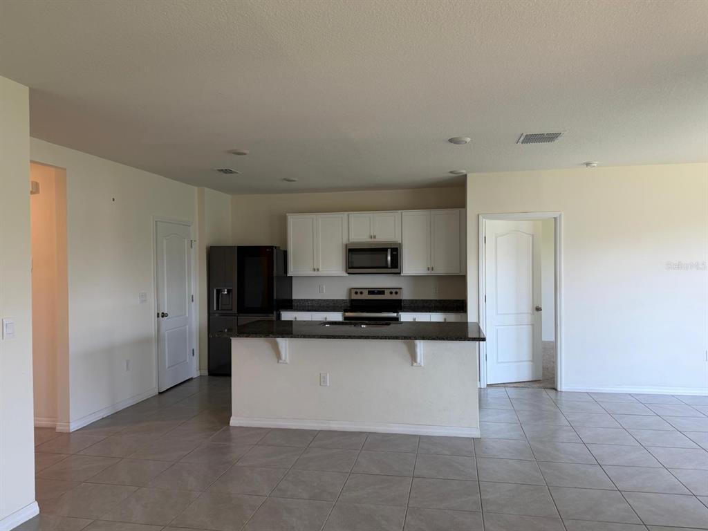 A kitchen features white cabinets, dark countertops, a kitchen island, and tile flooring — 4604 BERNARD BOULEVARD, HAINES CITY, FL