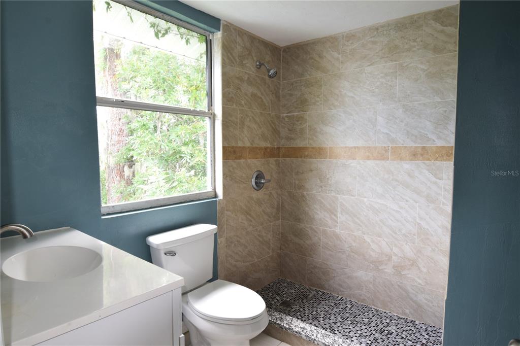 A bathroom features a tiled walk-in shower, a white vanity, and a toilet near a window — 941 HARTFORD AVENUE, DAYTONA BEACH, FL
