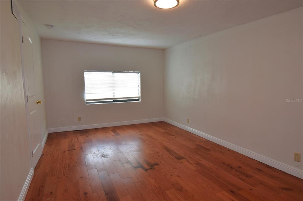 An empty bedroom features hardwood flooring, white walls, a window with blinds, and a ceiling light — 941 HARTFORD AVENUE, DAYTONA BEACH, FL